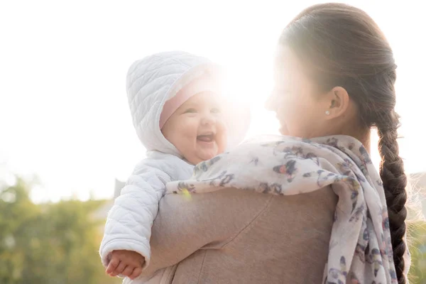 Neonati, infanzia, maternità, famiglia, stile di vita concetto felice giovane mamma in occhiali tenere grasso paffuto neonato sorridente bambina 6 mesi in giacca bianca all'aperto sullo sfondo di sole luminoso. — Foto Stock