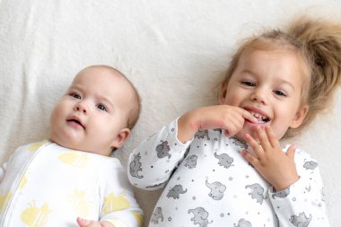 Yatakta birlikte oynayan gülümseyen küçük çocuklar. Erkek ve kız kardeş yeni doğmuş bir bebeğe oyuncak gösterir. Çocuklar yeni doğan kardeşlerle tanışıyor. Bebekler oynuyor ve kaynaşıyor. Küçük yaş farkları olan çocuklar. Boşluğu kopyala