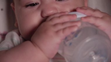 bebek, çocukluk, duygu konsepti - Kahverengi gözlü, yeni doğmuş, dişsiz bir bebeğin aşırı yakın plan gülümsemesi 7 aylık şişeden su içmesi ve bebek arabasında beyaz bir vücut giysisi içinde yatması