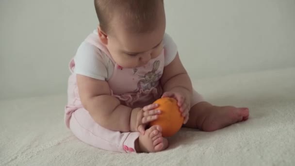 Criança, infância, comida, primeira alimentação, conceito de vitaminas - alegria criança playfull engraçado feliz 8 meses bebê menina come laranja. criança gordinha leva fruta doce e saborosa com as mãos dentro de casa no fundo branco — Vídeo de Stock