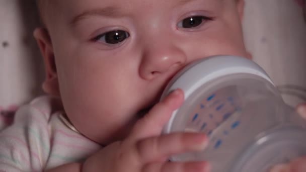 Infant, childhood, emotion concept - Extreme close-up of smiling face of brown-eyed newborn awake toothless baby 7 months old drink water from bottle with nipple lying in white bodysuit in stroller — Stock Video