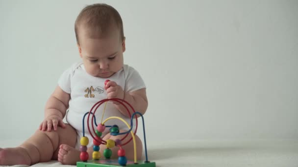 Bébé, concept d'enfance heureux drôle tout-petit enfant 8 mois bébé fille lécher jouer en bois Wired Bead Maze Abacus jeu sur fond blanc. chubby éveillé mineur assis rongeant jouet dans la salle de jeux à l'intérieur à la maison — Video