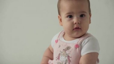 Bebek, çocukluk konsepti. Gülümseyen mutlu kahverengi gözlü, tombul çocuk uyandı. Neşesiz, dişsiz, 7 aylık bebek buruşuklukları, gözlerini kapatır evdeki beyaz arka planda yumuşak yatağa oturur.