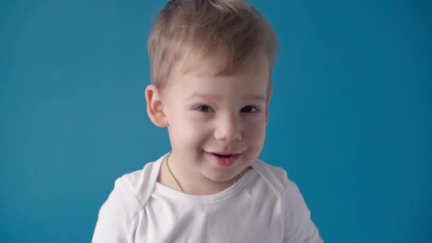 Filmagem de vídeo, felicidade, conceitos de infância - feliz, sorrindo, criança alegre pré-escolar menor Menino loiro posando olhar para a câmera, mostra caretas, danças, canta, palmas no fundo azul. — Vídeo de Stock