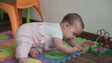 Bebek, çocukluk konsepti. Mutlu, komik, küçük bir çocuk. 8 aylık bebek kız, oturup tahta ve kablo boncuklu abaküs oyunu oynuyor. Tombul uyanık yeni doğmuş bebek oyun odasında, evde yerde sürünüyor.