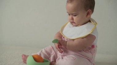 bebek, çocukluk, yemek, ilk beslenme, vitamin konsepti - neşe dolu oyun dolu çocuk Bib giysisi giymiş 8 aylık bebek tabaktan portakal yiyor. Beyaz arka planda kaşığı içeride olan tombul bir çocuk.