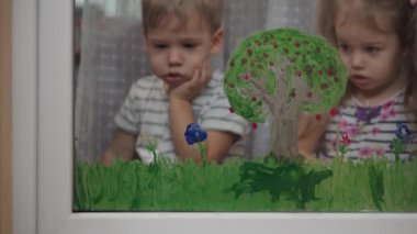 Çocukluk, yaratıcılık, doğa, ilkbahar, yaz konsepti - pencere camına akrilik renk çizen iki küçük anaokulu çocuğunun yakın çekimi. Kardeşlerin çocukları ve kız kardeşlerin manzara resimleri: ağaç, çimen
