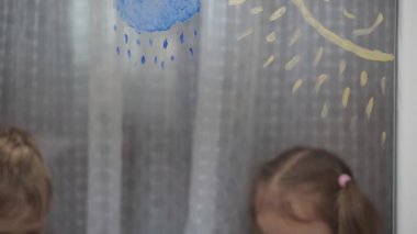 Çocukluk, yaratıcılık, doğa, ilkbahar, yaz konsepti - pencere camına akrilik renk çizen iki küçük anaokulu çocuğunun yakın çekimi. Kardeşlerin çocukları ve kız kardeşlerin manzara resimleri: ağaç, çimen