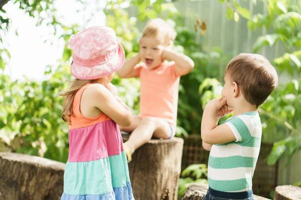 Three children of same age show different emotions. Kids in green garden play game deaf blind dumb outdoors in summer. sister and brothers show gesture of silence, hold finger to their lips, cover — Stockfoto