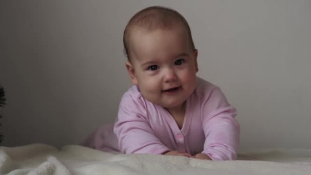 Criança, conceito de infância - close-up de sorrir feliz gordo retrato engraçado de olhos castanhos rosto gordinho de criança recém-nascida acordada. toothless 7 meses bebê grimaces, fecha os olhos mentira em cama macia em rosa na barriga. — Vídeo de Stock