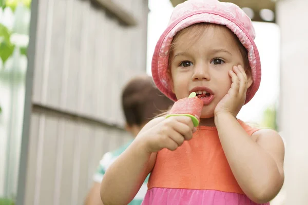 Summer, vacation, childhood, motherhood, food concept. Child has sore throat holding hand on cheeks, toothache. Kid aged 3 years eating popsicles in the garden outdoors. Happy children taste picnic