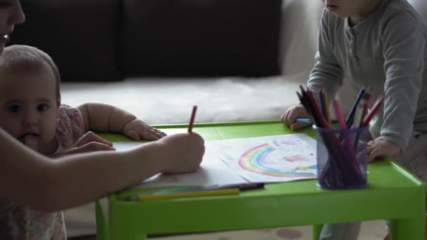 Infancia, arte, educación, creatividad, concepto de la maternidad auténtica madre joven con dos niños preescolar creativo talentoso niño de 2-4 años y bebé dibuja pinturas a lápices imagen sentarse a la mesa — Vídeos de Stock