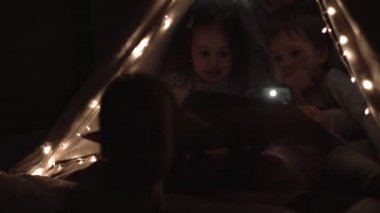 Otantik sevimli anne ve anaokulu çocukları evdeki çadırda kız ve erkek. Genç bir kadın 2-4 yaşlarındaki çocuklara kitap okurdu. Aile, Çocukluk, Annelik, Rahatlık ve Güvenlik kavramı