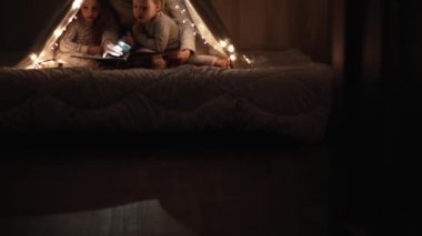 Otantik sevimli anne ve anaokulu çocukları evdeki çadırda kız ve erkek. Genç bir kadın 2-4 yaşlarındaki çocuklara kitap okurdu. Aile, Çocukluk, Annelik, Rahatlık ve Güvenlik kavramı