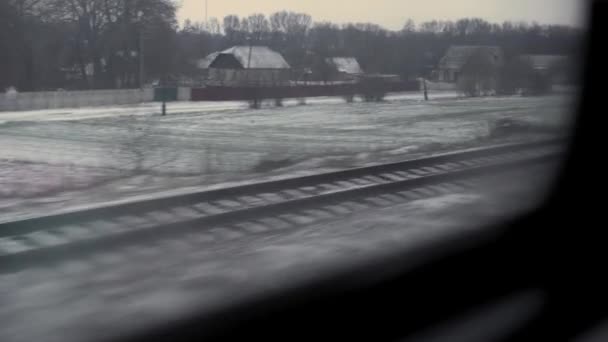 Транспорт, дорога, железная дорога, ландшафт, связь, концепция - вид из окна скоростного поезда на ландшафт заснеженного поля и леса во время зимней метели. Путешествие по сельской местности на поезде — стоковое видео
