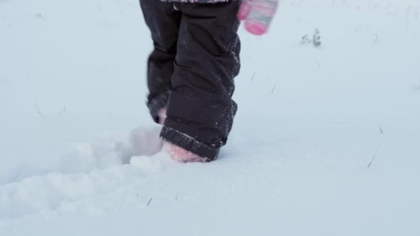 Winter, vacation, games, family concept - close up child runs through deep snow. children feet tread on snowy path. preschool toddler kid siblings dressed in black jumpsuit in snowfall in cold season — Stock Video