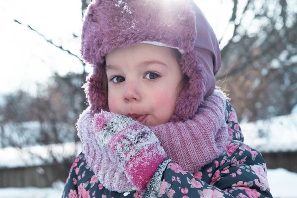 Winter, games, family, childhood concepts - close-up portrait authentic little preschool minor 3-4 years girl in pink hat look at camera posing smiles in snowy frosty weather. Funny kid eat taste snow