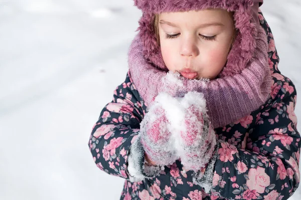 Winter, games, family, childhood concepts - close-up portrait authentic little preschool minor girl in pink hat warm clothes have fun smiles in cold frosty weather day. Funny kid blow on white snow
