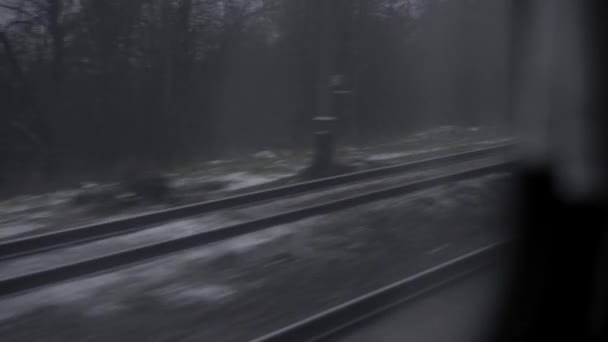Transporte, carretera, ferrocarril, paisaje, comunicación, concepto - vista desde la ventana del tren de velocidad en el paisaje de la naturaleza cubierto de nieve campo y bosque durante la tormenta de nieve de invierno. viajar en el campo por ferrocarril — Vídeos de Stock