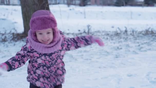 Зима, отдых, игры, семейная концепция - средний план аутентичного маленького дошкольного учреждения несовершеннолетней 3-4-летней девочки в фиолетовом на заснеженном лугу играет со снегом в предзакате. ребенок бегает по заснеженной местности — стоковое видео