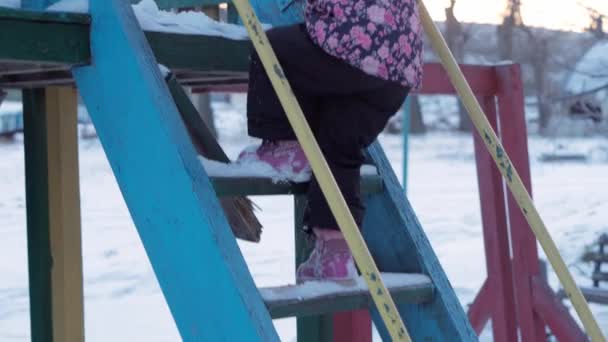 Zima, wakacje, gry, koncepcje rodzinne - środkowy plan autentycznego małego przedszkola małoletnia 3-4-letnia dziewczynka w fioletowym kolorze na pokrytej śniegiem łące schodzi po schodach na wieś. dziecko biegnie po śnieżnej okolicy — Wideo stockowe