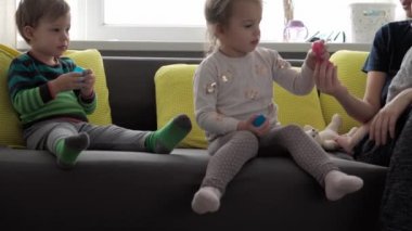 Mavi ve kırmızı sümüklü otantik bebek elleri. Kız ve oğlan anaokulunda yan yana oyun hamuru esnetiyorlar. Çocuk plastikçilik oynuyor. Modaya uygun sıvı oyuncak sarı kanepede el ve parmaklara yapışıyor.