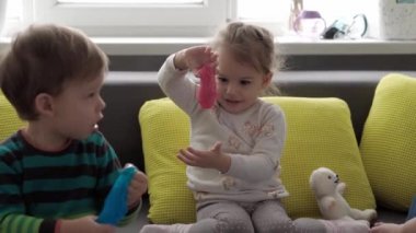 Mavi ve kırmızı sümüklü otantik bebek elleri. Kız ve oğlan anaokulunda yan yana oyun hamuru esnetiyorlar. Çocuk plastikçilik oynuyor. Modaya uygun sıvı oyuncak sarı kanepede el ve parmaklara yapışıyor.