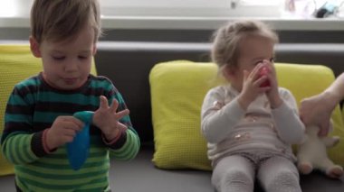 Mavi ve kırmızı sümüklü otantik bebek elleri. Kız ve oğlan anaokulunda yan yana oyun hamuru esnetiyorlar. Çocuk plastikçilik oynuyor. Modaya uygun sıvı oyuncak sarı kanepede el ve parmaklara yapışıyor.