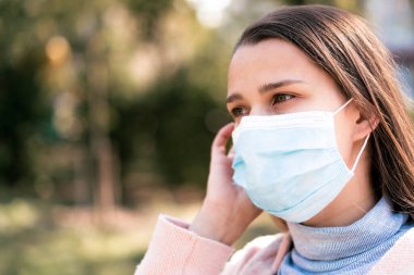 Bakım, bebekler, ilkbahar, koronavirüs ve karantina konsepti - Genç, uzun saçlı, Avrupa Kafkasyalı kadın, öğle vakti güneş ışığında mavi tıbbi koruyucu maske takıldı.