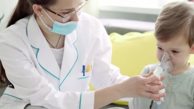 Genç kadın hemşire ya da doktor çocuk doktoru sarı gri kanepede 3-4 yıl anaokulu çocuğu için solunum prosedürü uyguluyor. Astım maskesi takmış şirin bir bebek. Hasta çocuğa iyi bak.