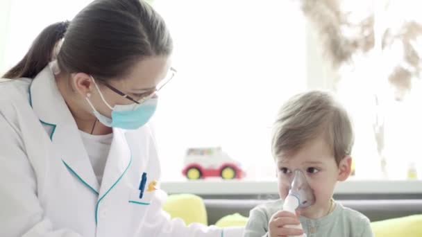 Primer plano de la enfermera joven o pediatra médico hace Procedimiento de inhalación para 3-4 años niño preescolar en el sofá gris amarillo. Lindo bebé en máscara de inhalador. cuidar de un niño enfermo — Vídeo de stock