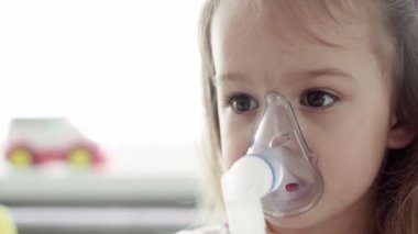 3-4 yaşlarında, sarı gri kanepenin üzerinde astım spreyi maskesi takmış, anaokulu öğrencisi bir çocuk. Bebek nebulizörle solunum terapisi görüyor. ilaç ve sağlık, pediatri, covid-19 konsepti