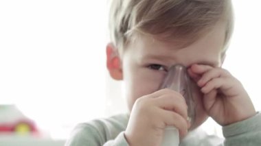 3-4 yaşlarında, sarı gri kanepenin üzerinde astım spreyi maskesi takan küçük bir anaokulu çocuğu. Bebek nebulizörle solunum terapisi görüyor. ilaç ve sağlık, pediatri, covid-19 konsepti
