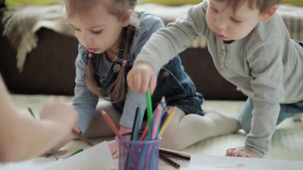 Otantik iki mutlu kardeş yaratıcı çocuklar anneleriyle birlikte kalemle çiziyorlar bahar geliyor resim gökkuşağı içeride, oyun odasında yerde eğleniyor. Çocukluk, Sanat, Eğitim, Yaratıcılık, annelik kavramı — Stok video