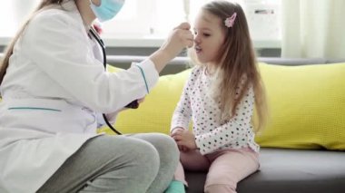 Genç kadın hemşire ya da doktor Kafkas Slav kökenli orta yaş planı sarı gri kanepede 3-4 yaş arası anaokulu öğrencisi kız çocuğuna iksir veriyor. ilaç ve sağlık, pediatri, covid-19 konsepti