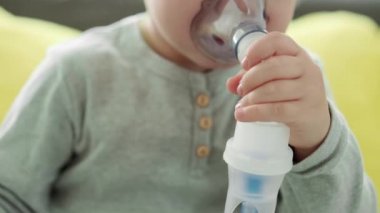 3-4 yaşlarında, sarı gri kanepenin üzerinde astım spreyi maskesi takan küçük bir anaokulu çocuğu. Bebek nebulizörle solunum terapisi görüyor. ilaç ve sağlık, pediatri, covid-19 konsepti