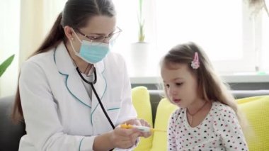 Beyaz Slav kadın hemşire ya da doktor çocuk doktorunun orta dereceli planı sarı kanepede 3-4 yaş arası anaokulu öğrencisi bir çocuğun vücut ısısını ölçmek. ilaç ve sağlık, pediatri, covid-19 konsepti