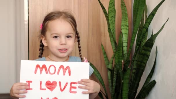 Närbild söt liten förskola kaukasiska flicka 3-4 år håller vitt lakan med förklaring av kärlek mamma. Unga dotter ler kär visar hjärta symbol med händer. Romantiskt koncept för mödradagen. — Stockvideo