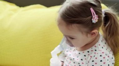 3-4 yaşlarında, sarı gri kanepenin üzerinde astım spreyi maskesi takmış, anaokulu öğrencisi bir çocuk. Bebek nebulizörle solunum terapisi görüyor. ilaç ve sağlık, pediatri, covid-19 konsepti