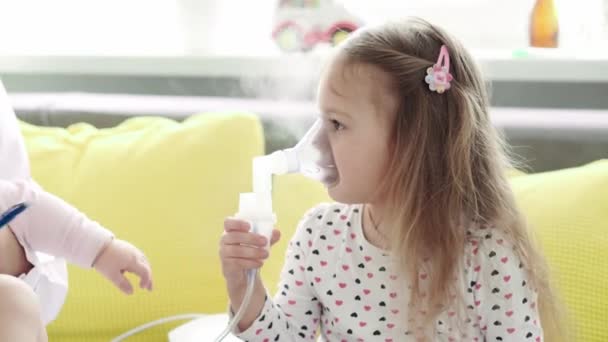 Primer plano de la enfermera joven o pediatra médico hace Procedimiento de inhalación para niños de 3-4 años niña preescolar en el sofá gris amarillo. Lindo bebé en máscara de inhalador. cuidar de un niño enfermo — Vídeo de stock