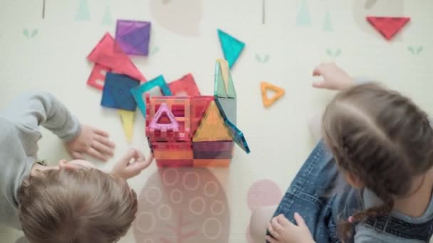 Barndom, familj, moderskap koncept - ovanifrån unga glada Barn njuta av att spela kreativa spel magneter block bygger slott. Träd Barn syskon har kul tillsammans i lekrummet golvet på karantän — Stockvideo