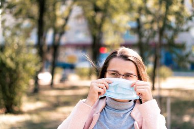 Bakım, bebekler, ilkbahar, koronavirüs ve karantina konsepti - Genç, uzun saçlı, Avrupa Kafkasyalı kadın, öğle vakti güneş ışığında mavi tıbbi koruyucu maske takıldı.