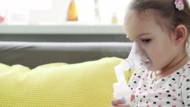 3-4 yaşlarında, sarı gri kanepenin üzerinde astım spreyi maskesi takmış, anaokulu öğrencisi bir çocuk. Bebek nebulizörle solunum terapisi görüyor. ilaç ve sağlık, pediatri, covid-19 konsepti