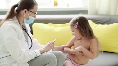 Beyaz tenli genç, tatlı, Slav kadın hemşire ya da doktor çocuk doktorunun orta dereceli planı sarı gri kanepede 3-4 yaş arası anaokulu öğrencisi çıplaklığı aşıladı. ilaç ve sağlık, pediatri, covid-19 konsepti