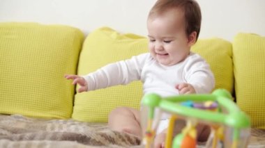 bebeklik, çocukluk, ebeveynlik, gelişim, ilaç ve sağlık konsepti - yakın plan bebek tombul bebek beyaz beden giysisi içinde neşeli uyanıklık sarı koltukta oturan çok renkli oyuncakla gülümsüyor