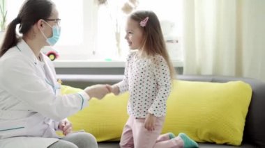 Kafkas Slav kökenli genç kadın hemşire veya doktor çocuk doktorunun orta dereceli planı, sarı gri kanepede 3-4 yaşındaki anaokulu öğrencisi kızı muayene ediyor. ilaç ve sağlık, pediatri, covid-19 konsepti