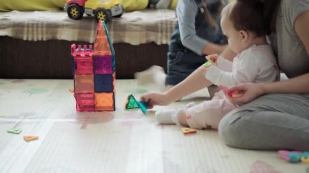Childhood, family, motherhood, parenthood concept - young happy mother spends time playing magnets blocks builds castle with toddler kids. Joy Children have fun together in playroom floor on — Stock Video