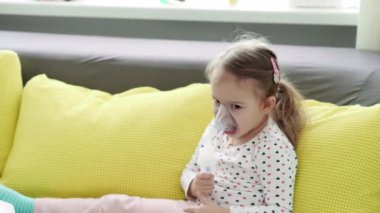 3-4 yaşlarında, sarı gri kanepenin üzerinde astım spreyi maskesi takmış, anaokulu öğrencisi bir çocuk. Bebek nebulizörle solunum terapisi görüyor. ilaç ve sağlık, pediatri, covid-19 konsepti