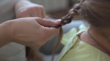 Otantik, genç, beyaz bir kadın annesi, çocuk örgüleriyle ilgileniyor sarı saçlı sarı saçlı kız örgüleri, gri kanepe üzerinde. Örgü örme işlemi. Moda ve güzellik, annelik kavramı.