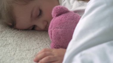 3-4 yıl boyunca tatlı beyaz bir yatakta oyuncak ayıyla tatlı tatlı tatlı uyuyan, beyaz, küçük beyaz bir anaokulu çocuğunun otantik yakın çekimi. Çocuk bakımı, Uyuyan Bebek, Çocukluk, Ebeveynlik, Yaşam Konsepti